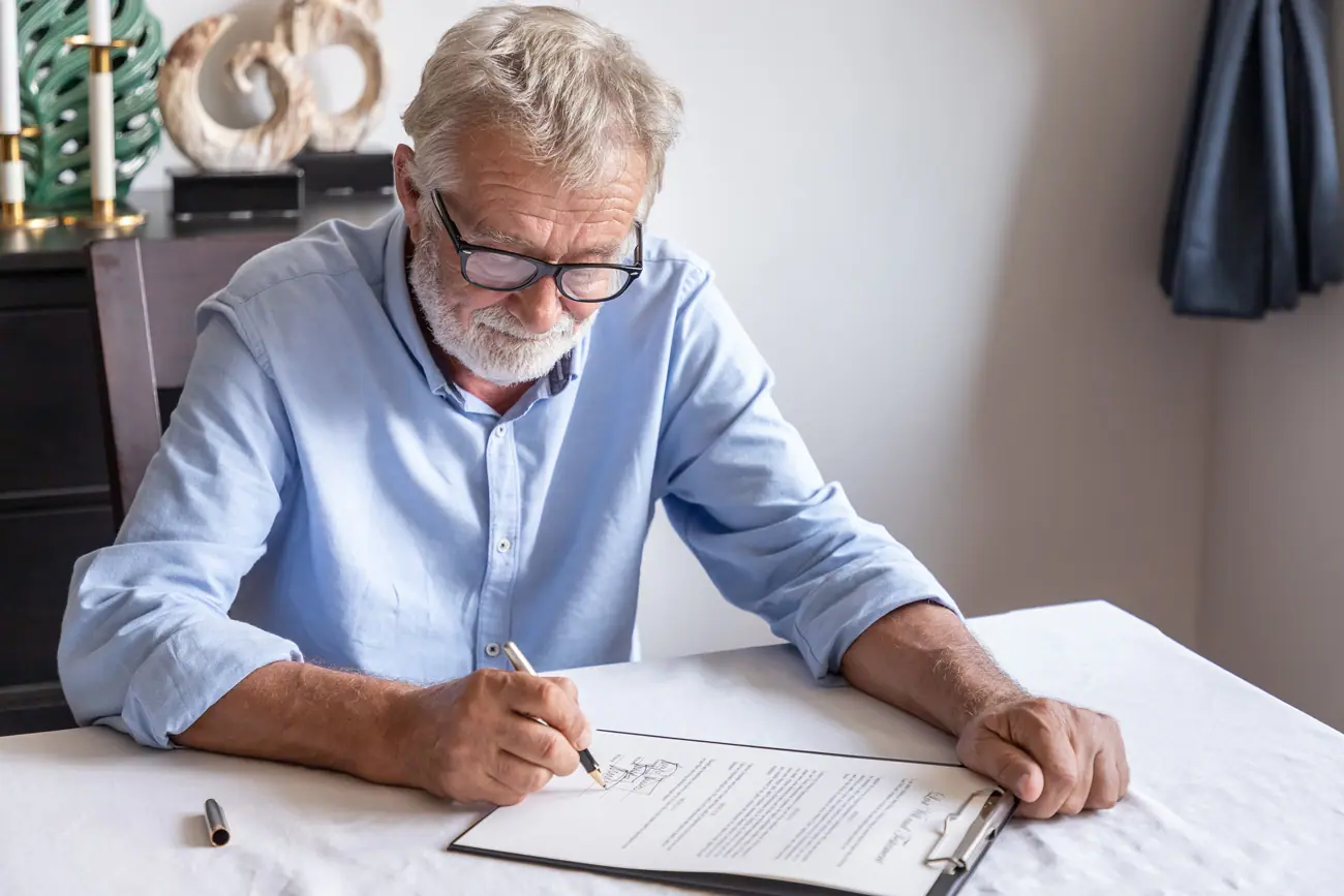 Older man in a blue shirt signing legal documents related to probate, emphasizing the importance of proper estate management and legal guidance in Texas.